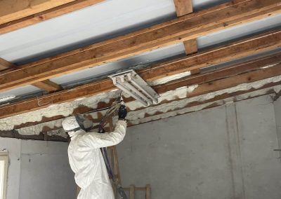 Proces izolacije garaže poliuretanskom penom. Radnik nanosi belu izolacionu penu na unutrašnje zidove garaže, stvarajući ravnomerni sloj za poboljšanu toplotnu izolaciju.