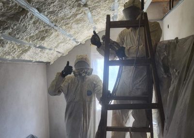 Unutrašnjost stambene kuće sa sveže izolovanim krovom. Poliuretanska pena ravnomerno prekriva celokupnu površinu krovne konstrukcije, pružajući odličnu toplotnu zaštitu. U prvom planu se vidi deo prostorije sa izolovanim krovom