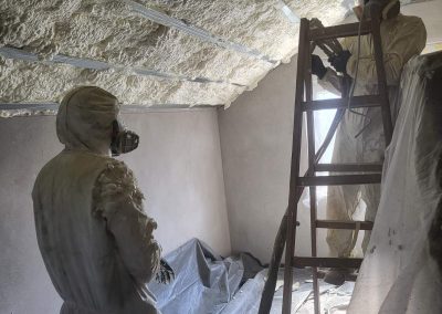 Unutrašnjost stambene kuće sa sveže izolovanim krovom. U prvom planu su radnici, a iza njih se vidi rezultat njihovog rada - poliuretanska pena koja ravnomerno prekriva celokupnu površinu krovne konstrukcije. Izolacija pruža odličnu toplotnu zaštitu, povećavajući energetsku efikasnost doma